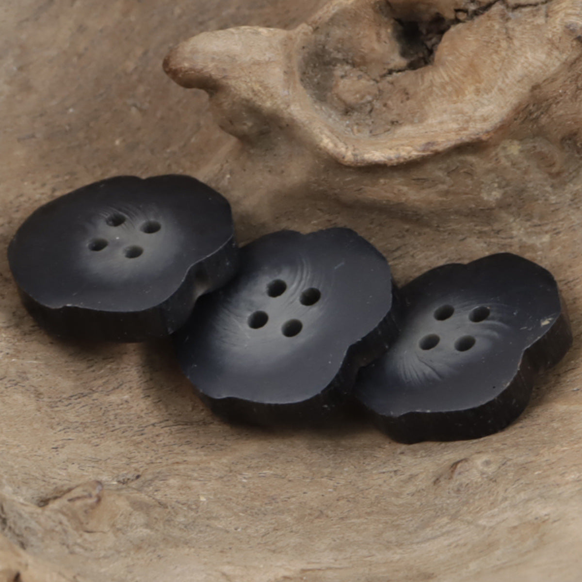 Three irregular matte black resin buttons, four-hole tops, stacked close-up.