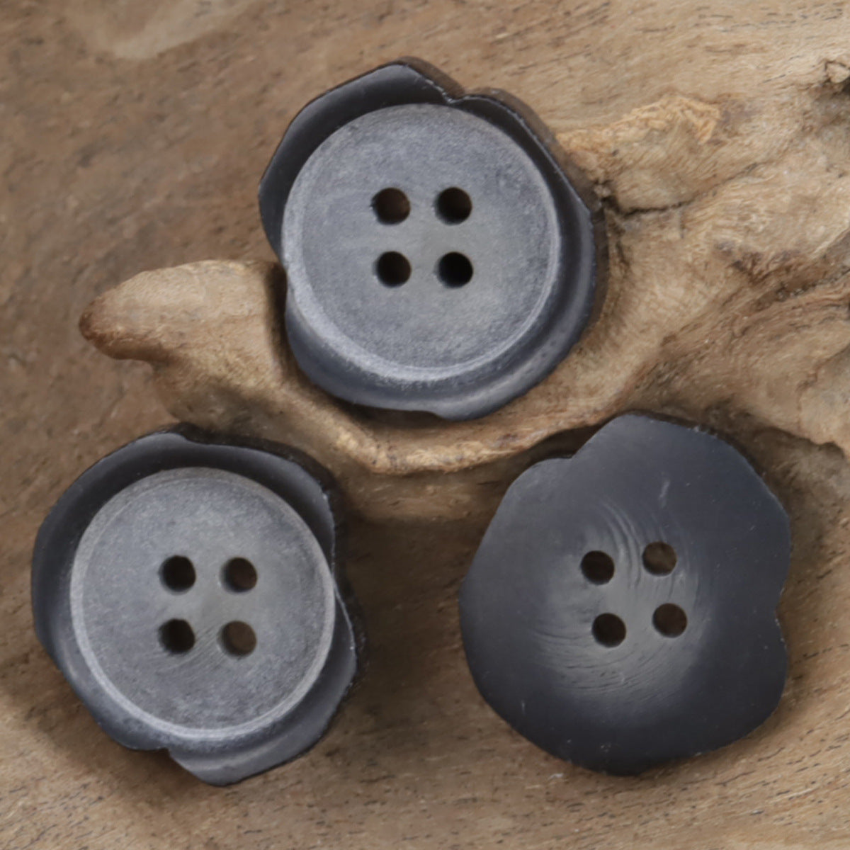 Set of irregular matte black resin buttons, four-hole fronts, angled view.