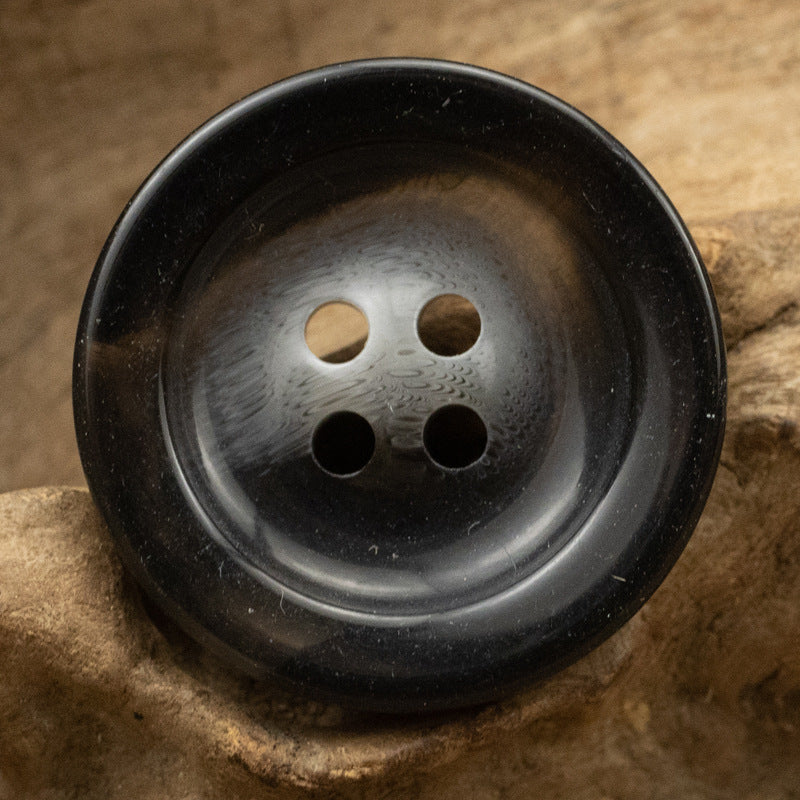 Round 4-hole resin button, black glossy with mixed lighter hole edges.