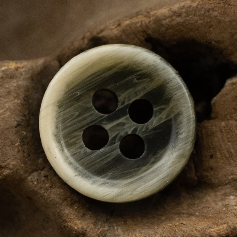 Light cream resin shirt button with 4 holes, faint gray-green textured pattern