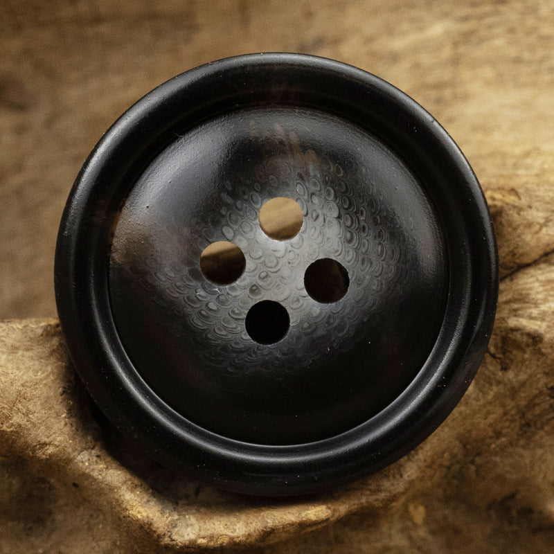 Dark resin button with off-center 4-hole openings and mottled texture