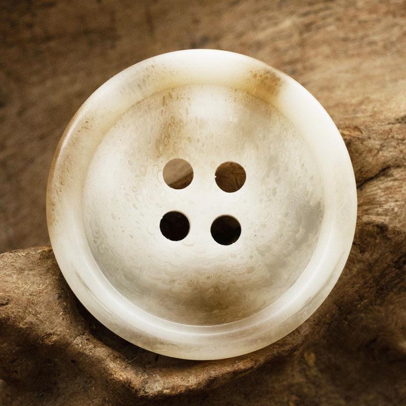 Off-white resin button with 4-hole face and warm mottled swirl texture