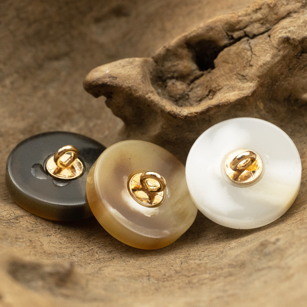 Resin buttons close-up: dark, tan, and white rounds with gold shanks