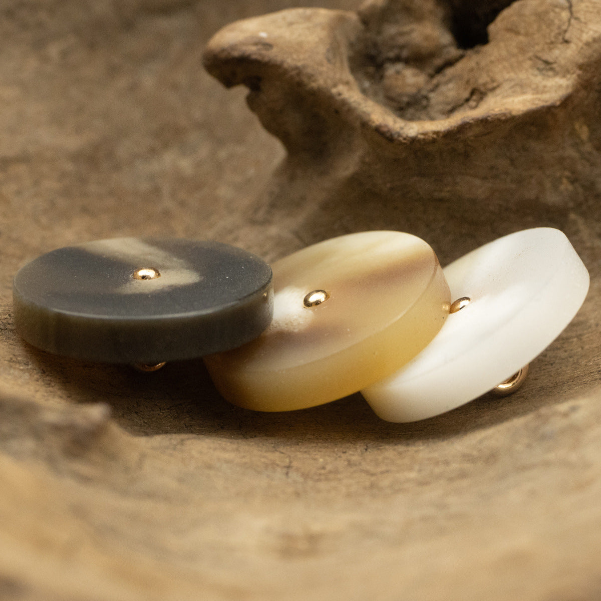 Resin buttons side view: dark gray, tan, and white with gold metal shanks