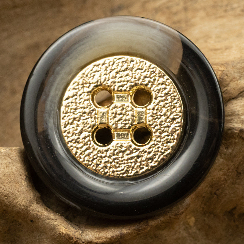 Black round resin button with gold textured center, gold metal rim and four holes