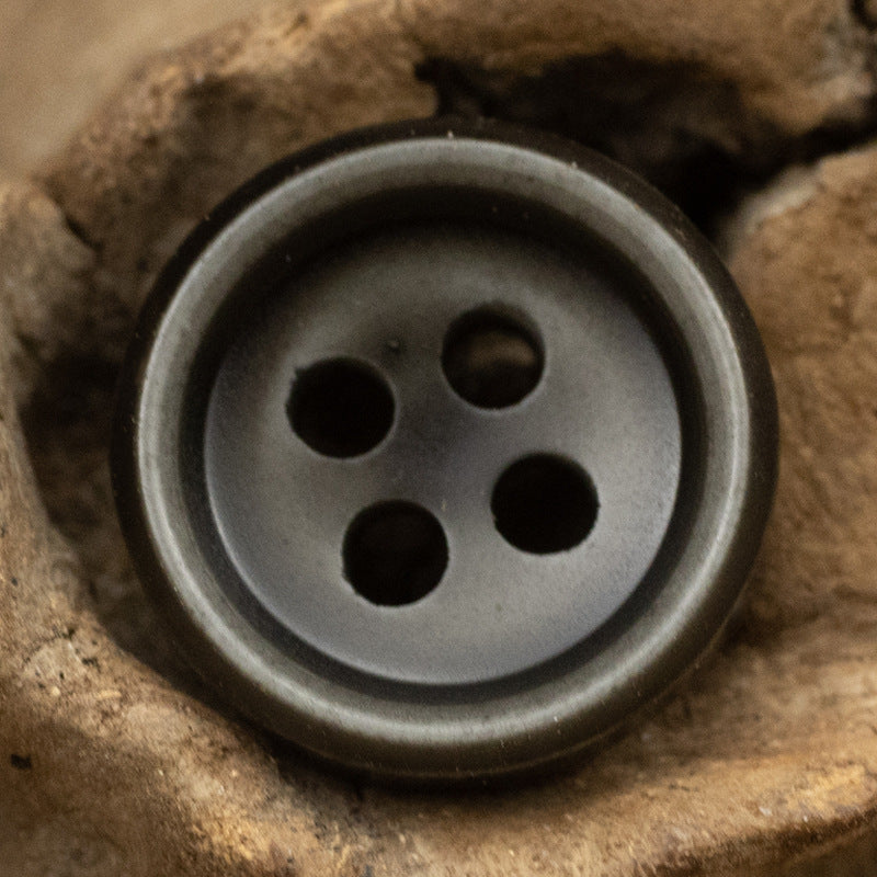 Gray resin button with four holes and a smooth rim