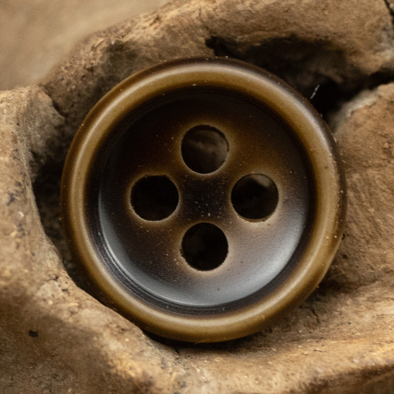 Dark resin button with four holes and a bronze-toned edge