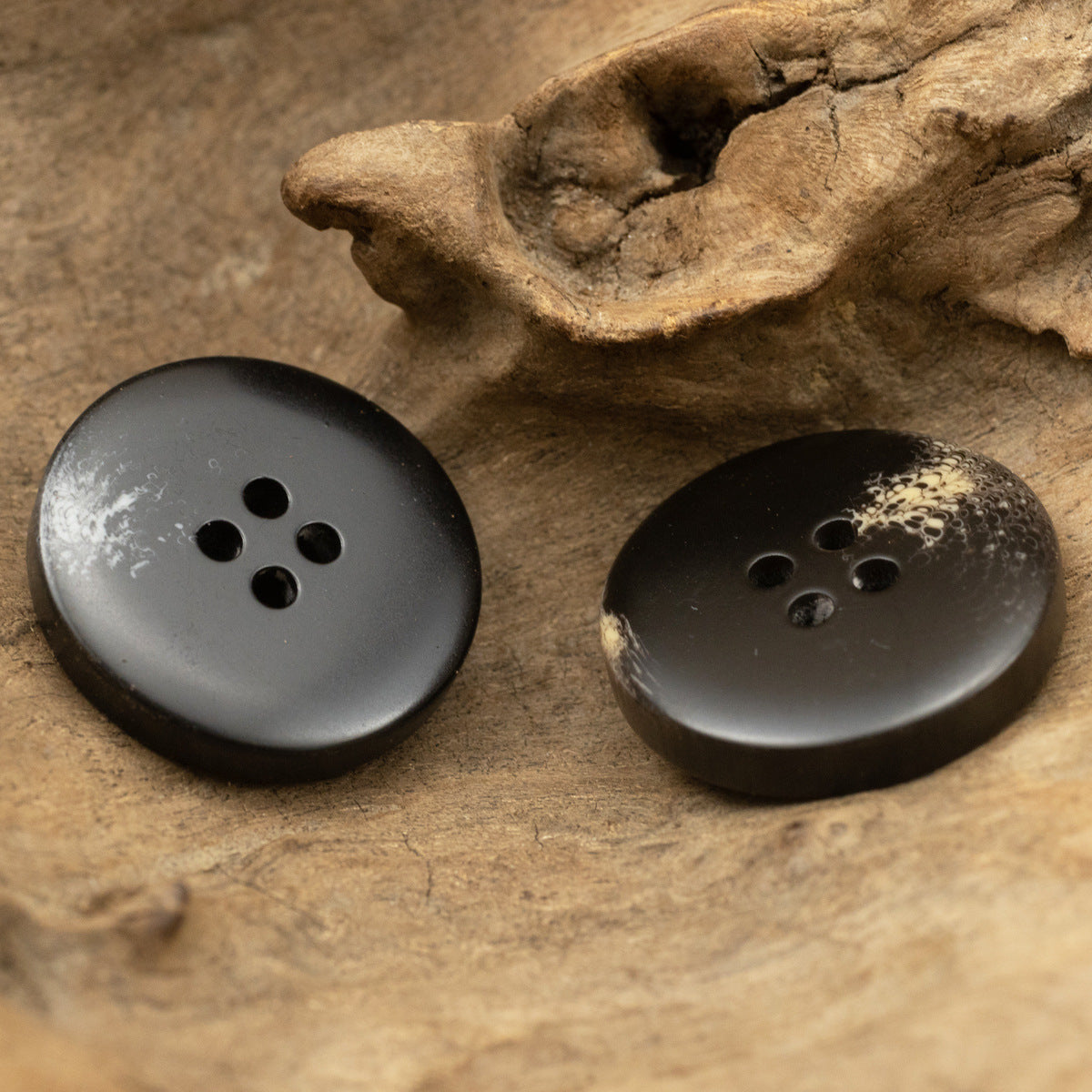 Black resin coat buttons, 4-hole, pair on stone texture, close-up