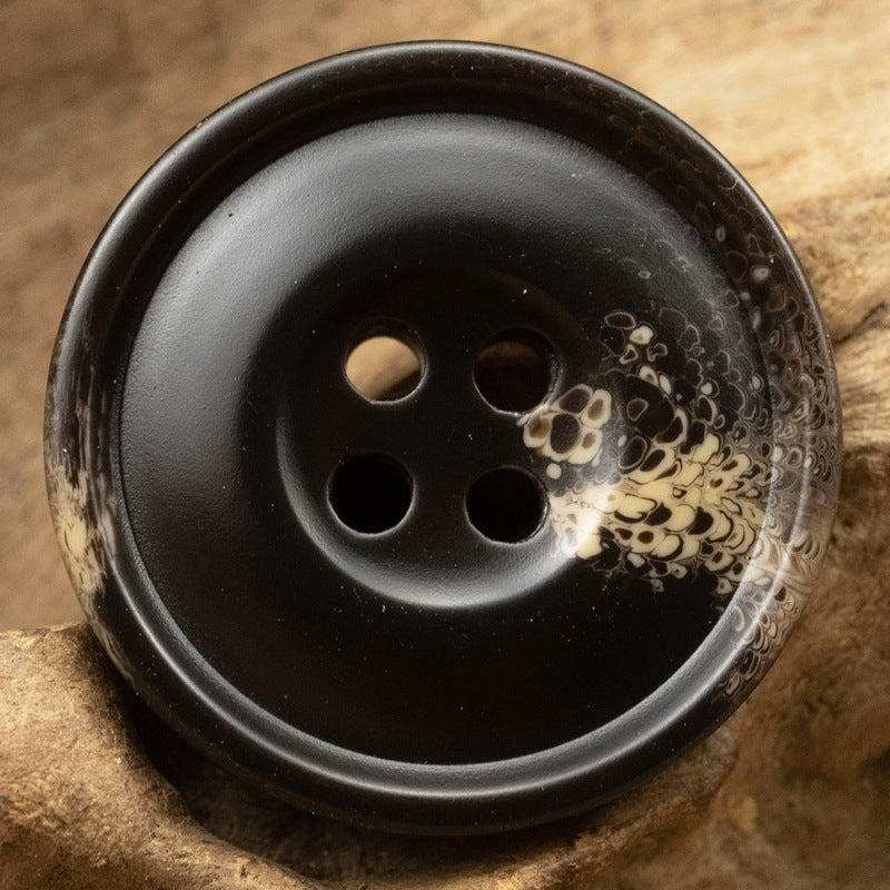 Black resin coat button, 4-hole, speckled floral pattern on face, close-up