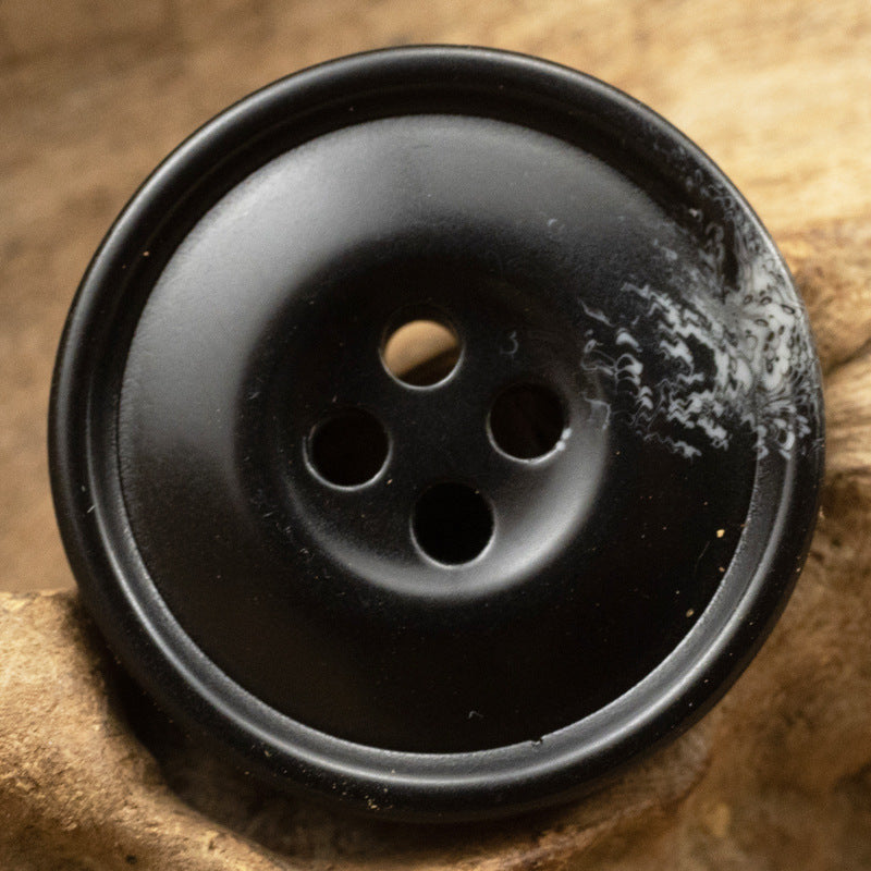 Black resin coat button, 4-hole, smooth face with subtle speckling, close-up