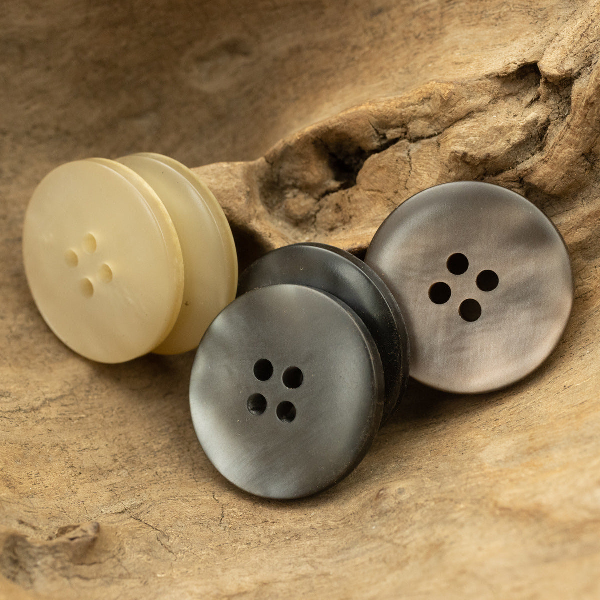 Three circular 4-hole buttons in cream, gray, and dark tones with smooth wood grain