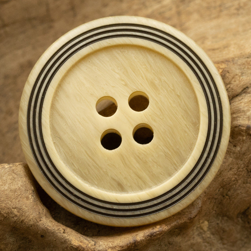 Light cream circular 4-hole button with wood-grain texture and triple-ring striped edge