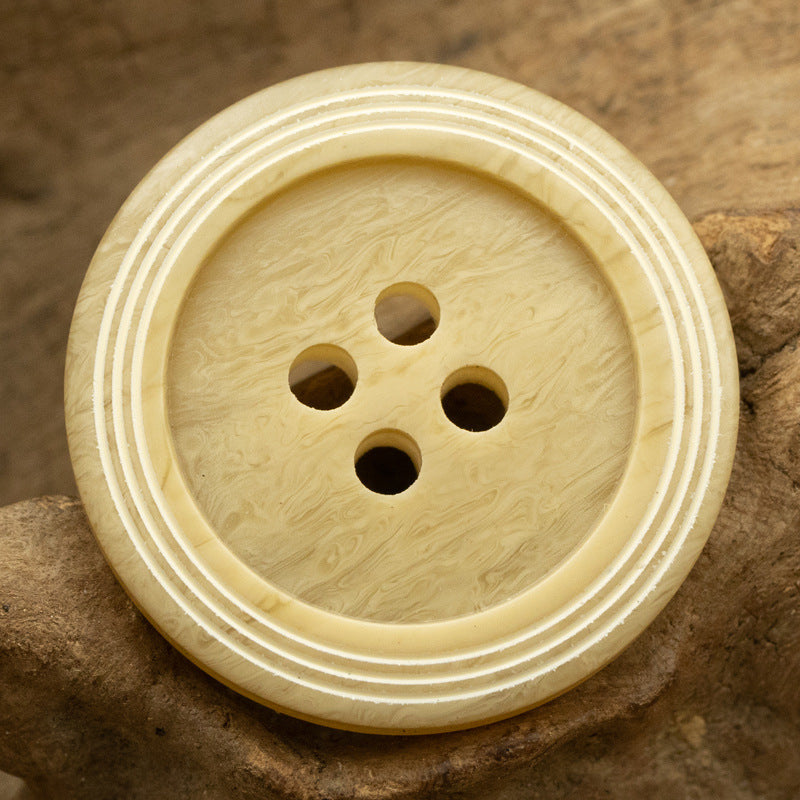 Light khaki yellow circular 4-hole button with wood-grain texture and triple-ring striped edge