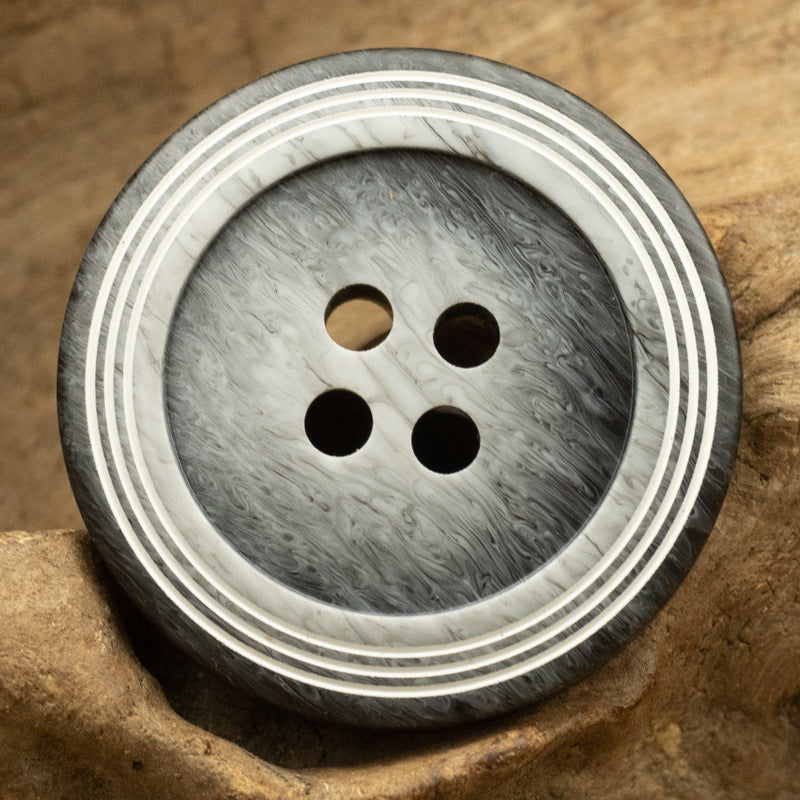 Gray circular 4-hole button with wood-grain texture and triple-ring striped edge
