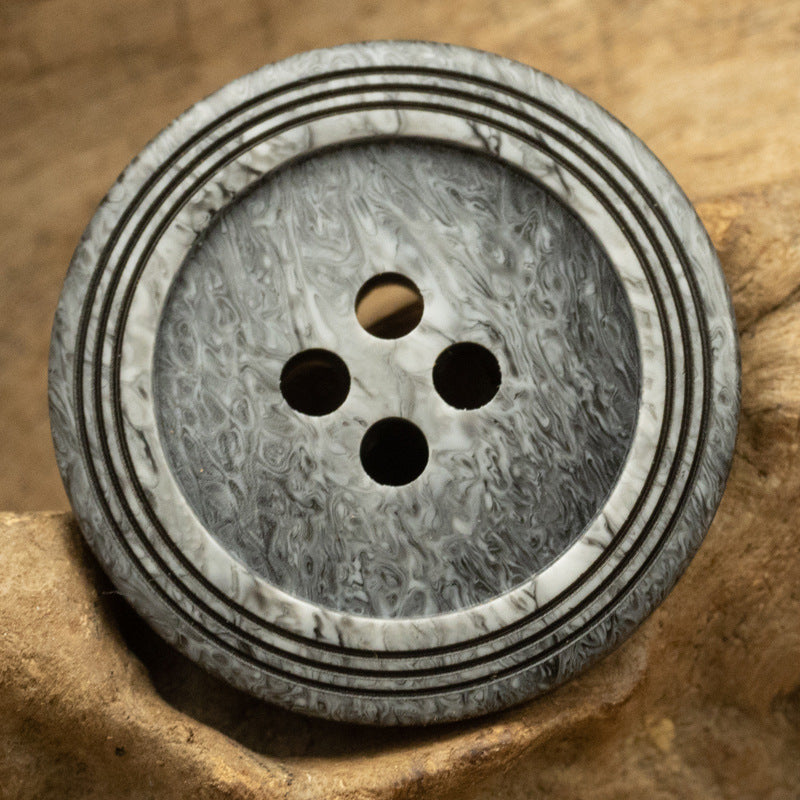 Dark gray circular 4-hole button with wood-grain texture and triple-ring striped edge