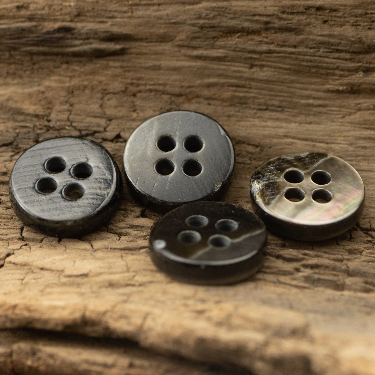 Four 4-hole round buttons on wood, mixed silver and iridescent finishes.