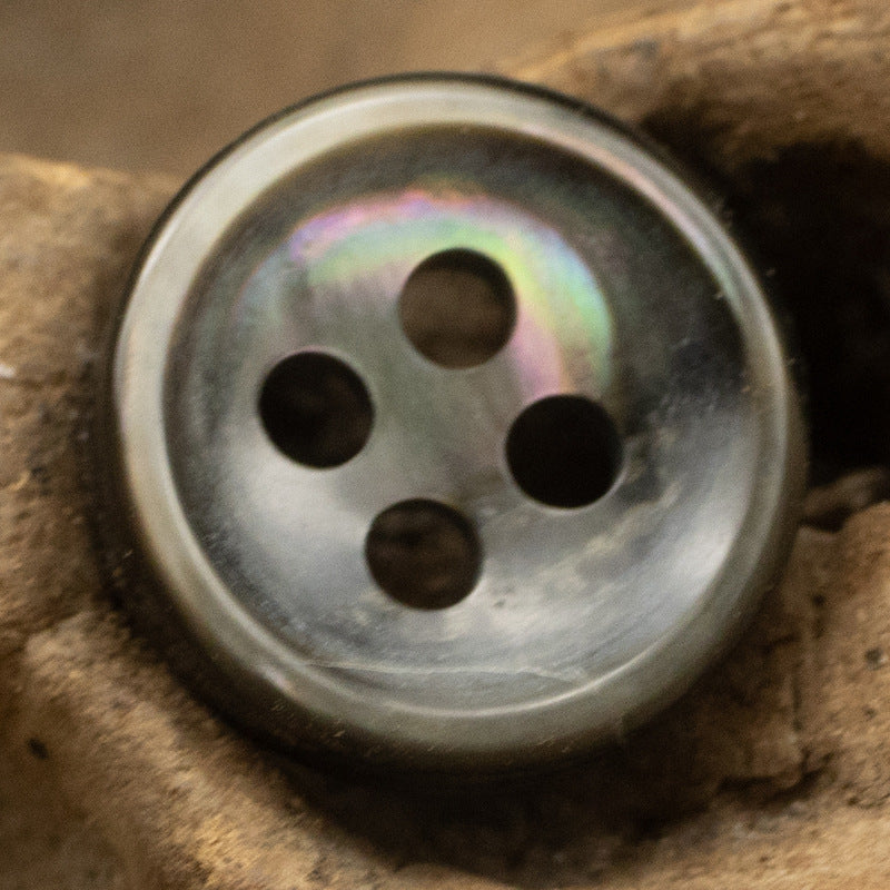 Close-up: iridescent pearl-look 4-hole round button, silvery gray body.
