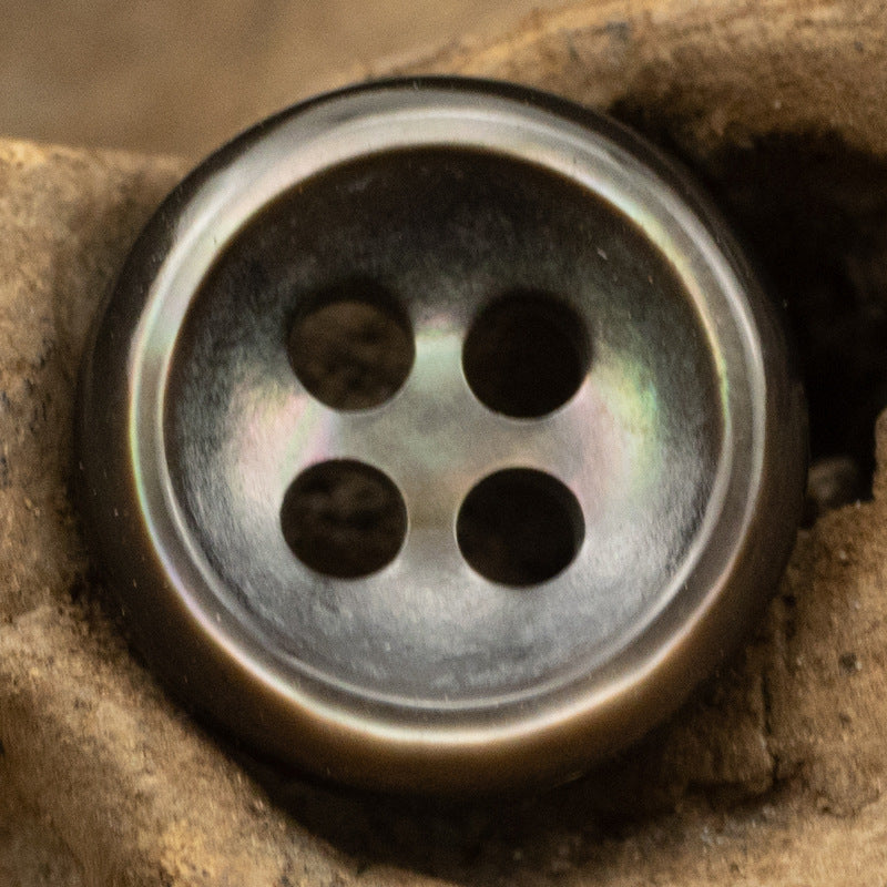 Close-up: dark pearl-look round button with 4 holes and subtle rainbow sheen.