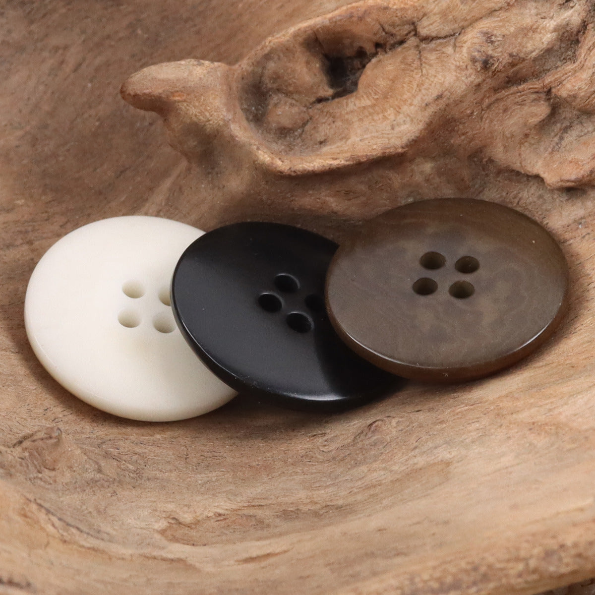 Three suit buttons: white, black, and brown, each with four holes