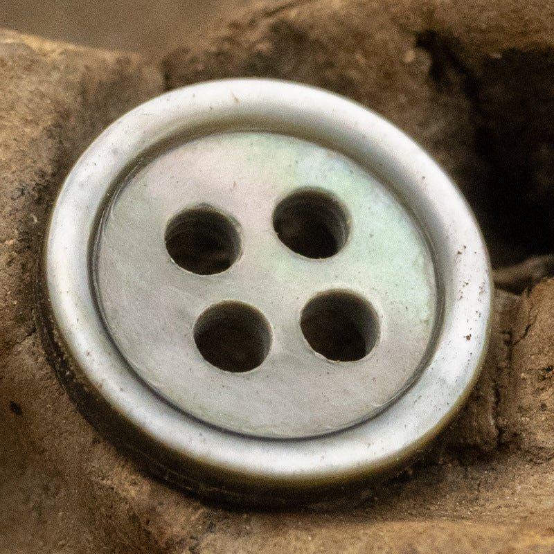 Round 11.5mm shell button, 4-hole—light pale blue/gray tone with mottled edges.