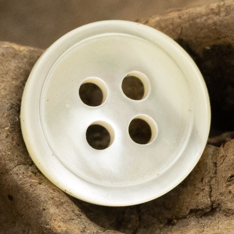 Round 11.5mm shell button, 4-hole—light cream/off-white with dark button holes (close-up).