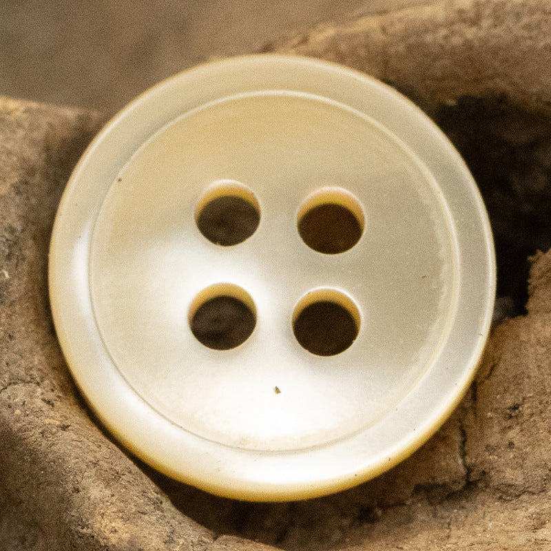 Round 11.5mm shell button, 4-hole—light beige with darker holes (close-up).