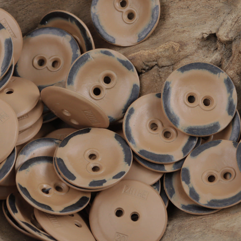 Two-hole metal buttons in beige/khaki tones with dark speckle edges, scattered