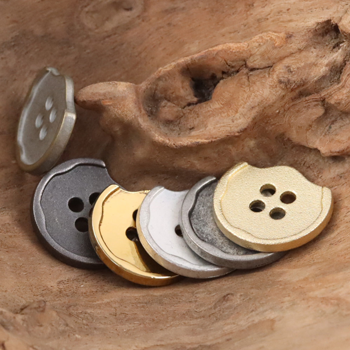 Stack of irregular metal buttons in gray, cream and gold tones, each with 4 holes