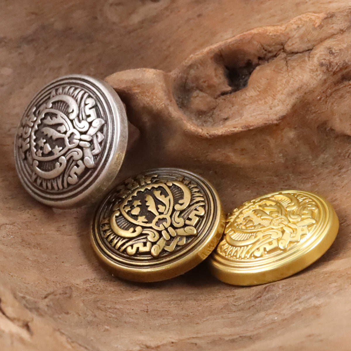 Three round metal shield buttons in silver, bronze, and gold tones with ornate emblem