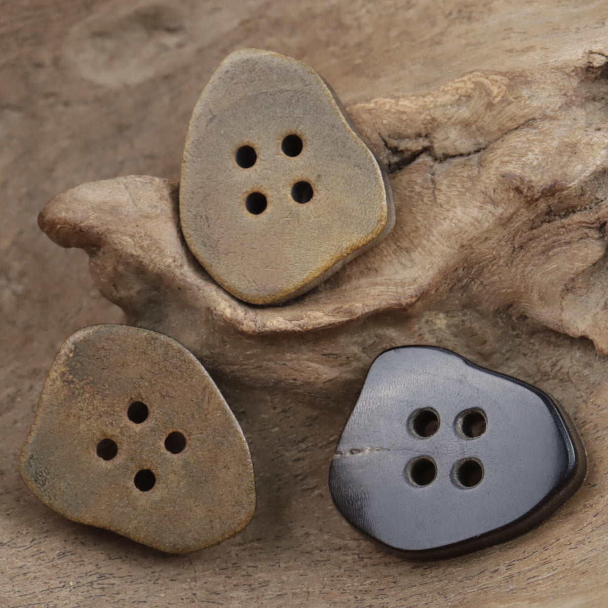 Irregular horn buttons in tan and dark gray, each with four stitch holes.