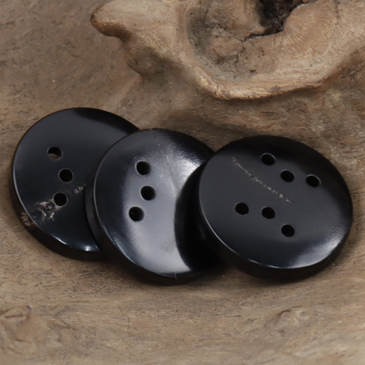 Round black six-hole buttons, side view with metal-like sheen and stitched texture