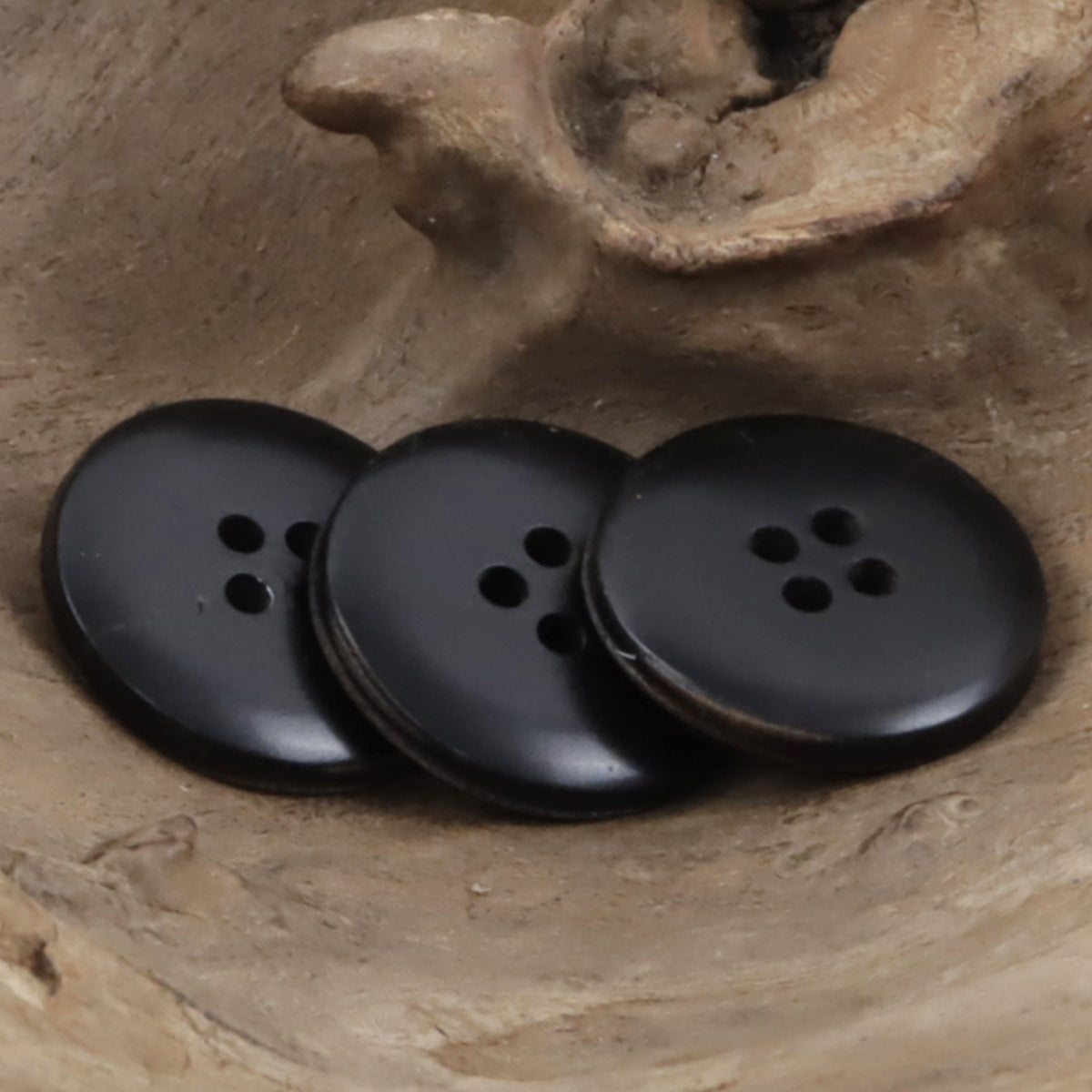 Three black round cow horn buttons with four-hole fronts and stitched seams.