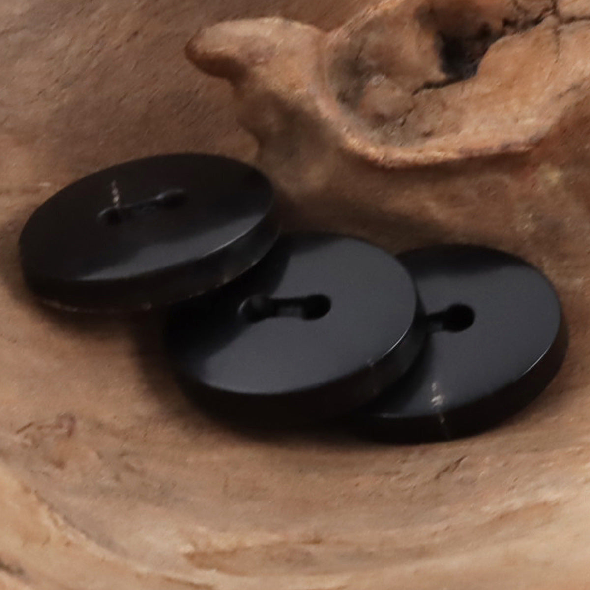 Black horn buttons with bevel-cut surface texture and split-eyelet holes, close-up