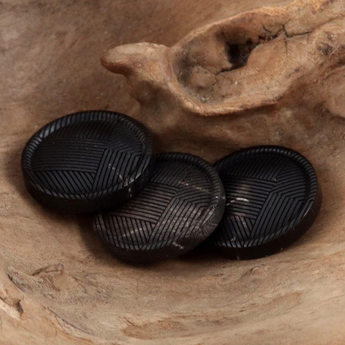 Three black round buttons showing raised geometric stripe pattern on the front