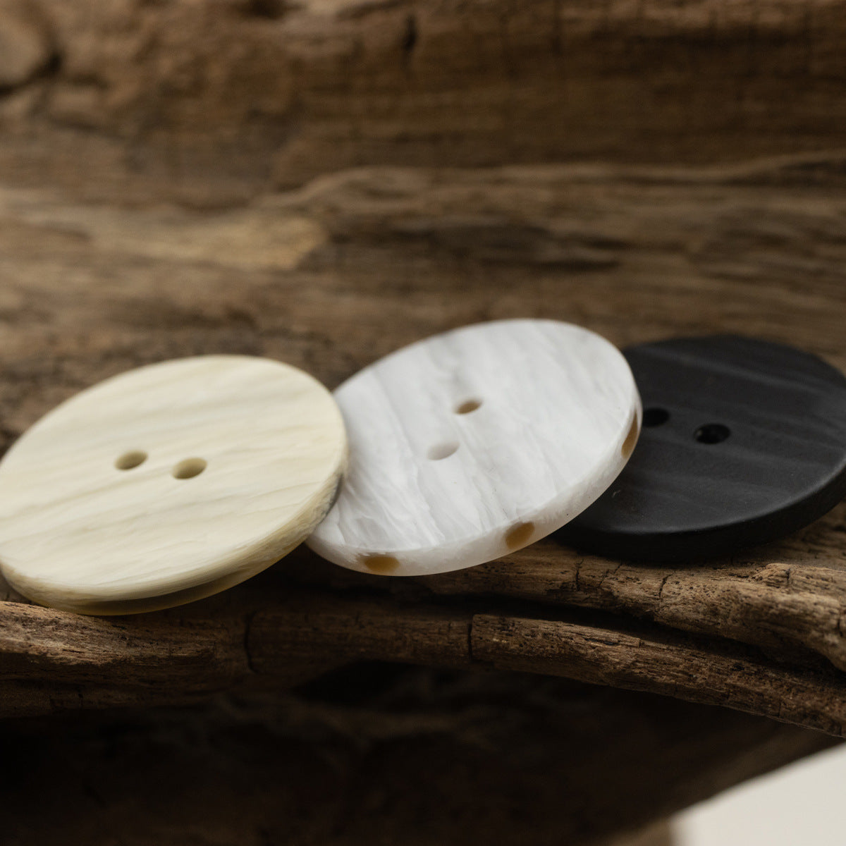 Flat 2-hole resin buttons in off-white, light khaki and black on wood