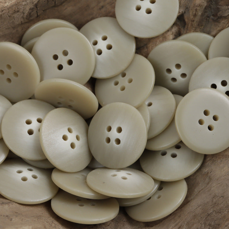 Light beige round resin buttons with 4-hole faces, mixed in a pile