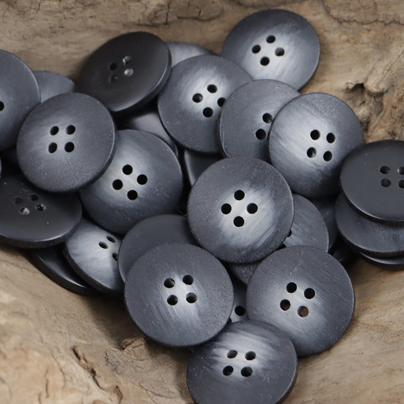 Dark gray round resin buttons with 4-hole design, stacked in a pile