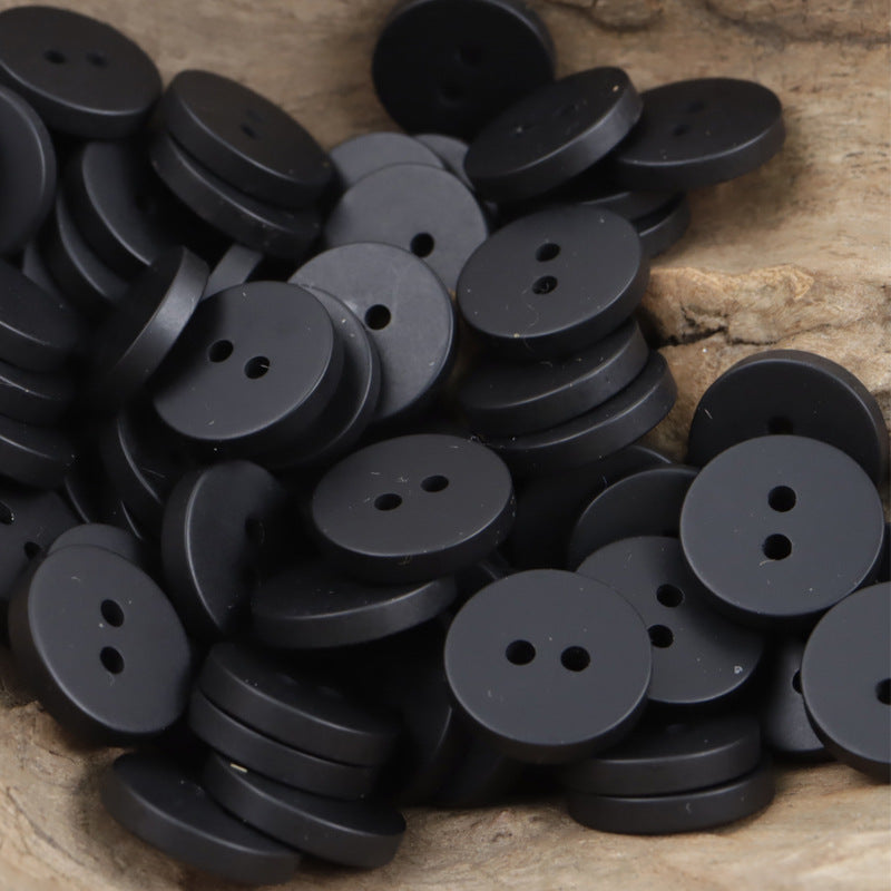 Dark gray/black two-hole round resin buttons, stacked in a pile