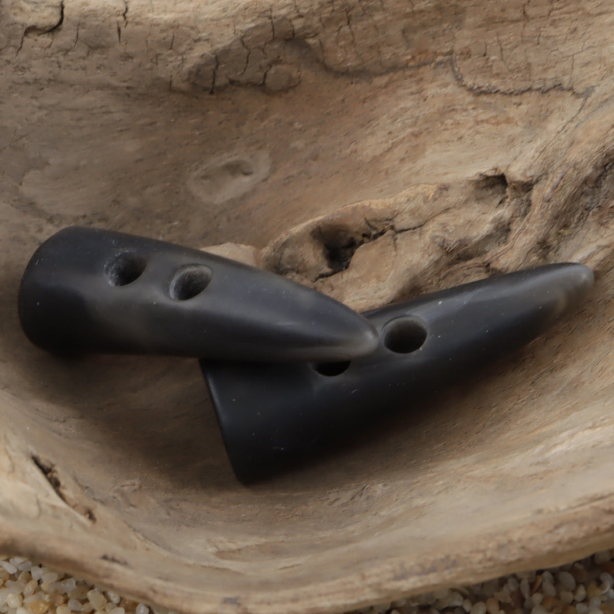 Two dark horn-shaped resin toggle buttons with curved ends and round holes