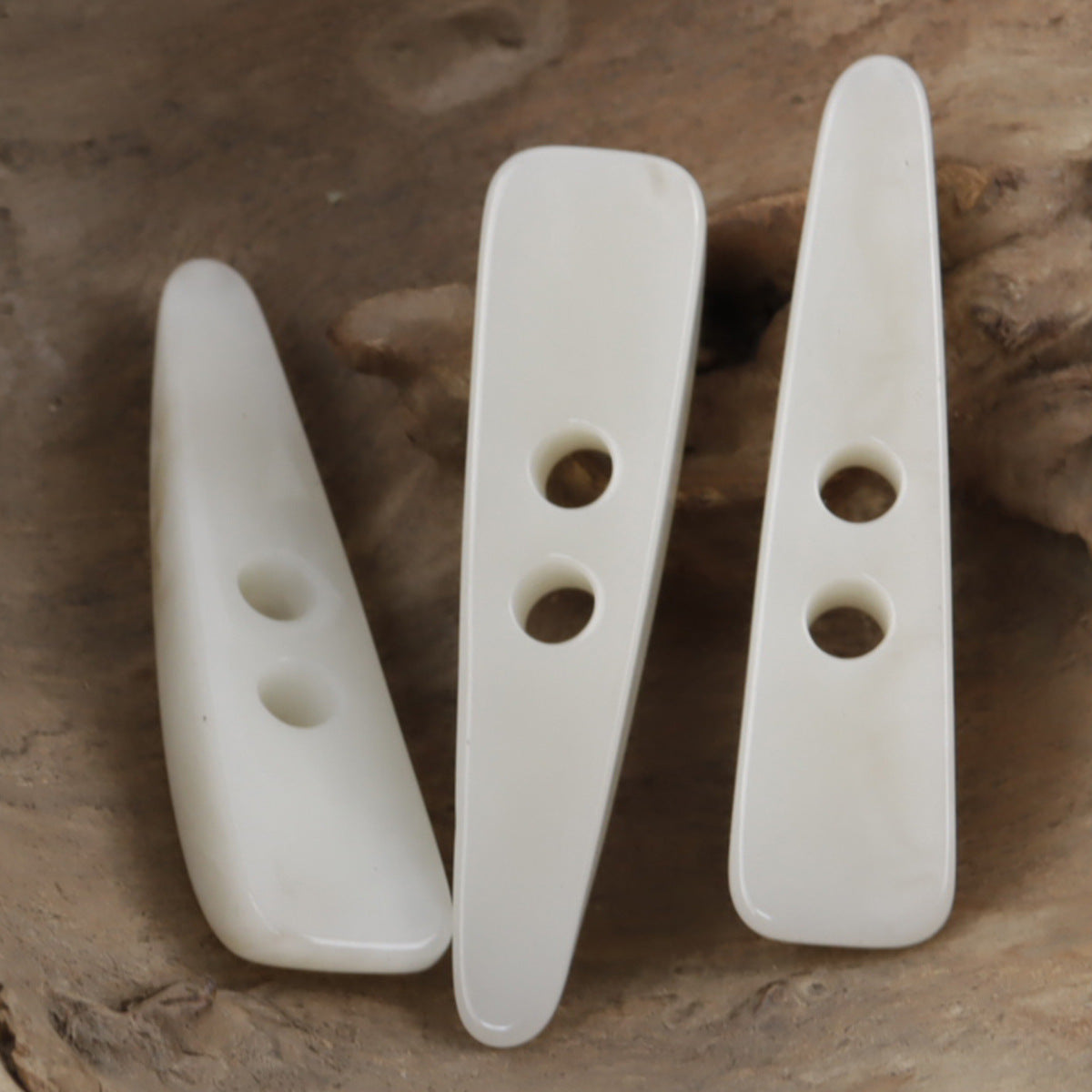 White resin horn-shaped toggle buttons with oval openings and round holes