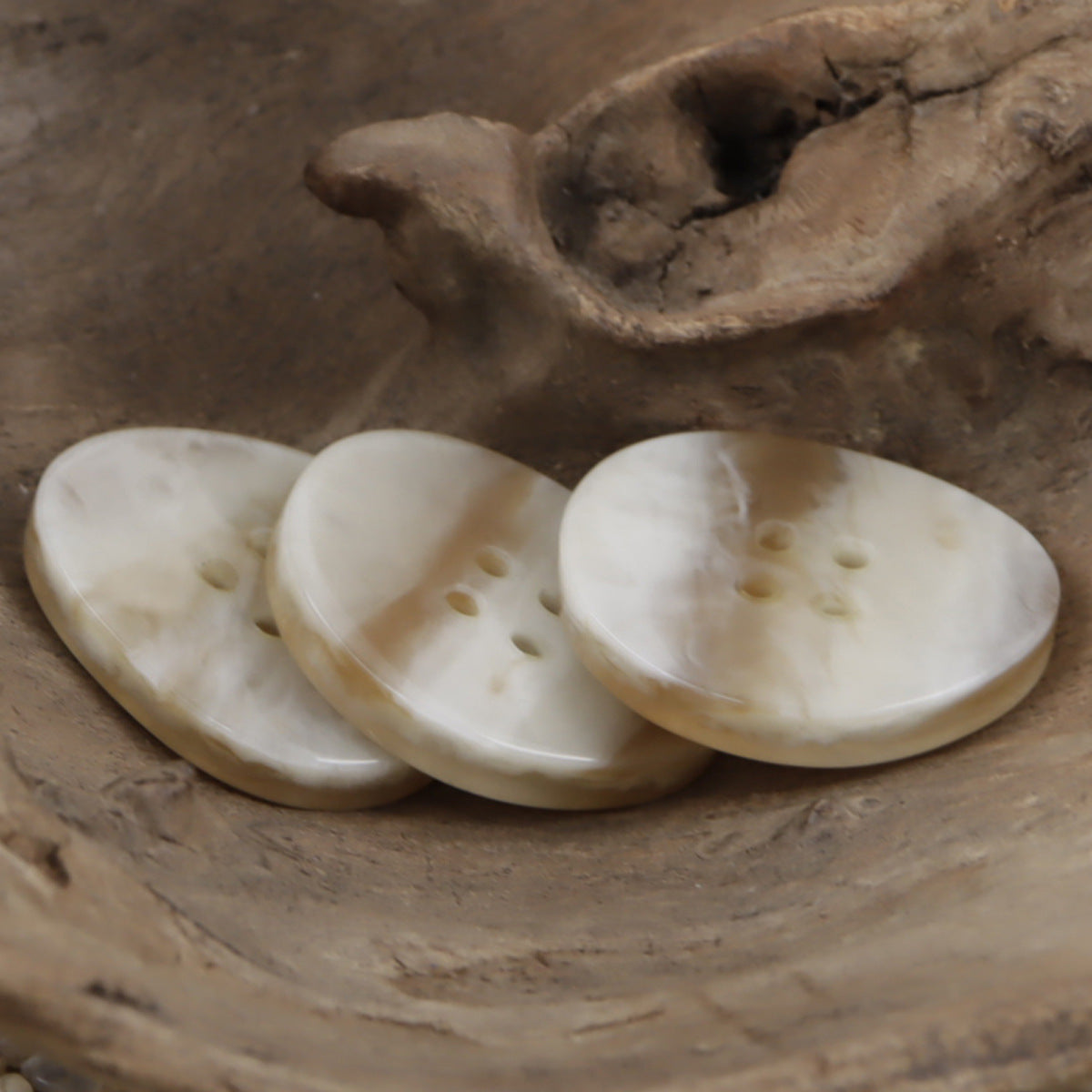 Row of light khaki 4-hole resin buttons, irregular oval, wood-grain pattern and holes