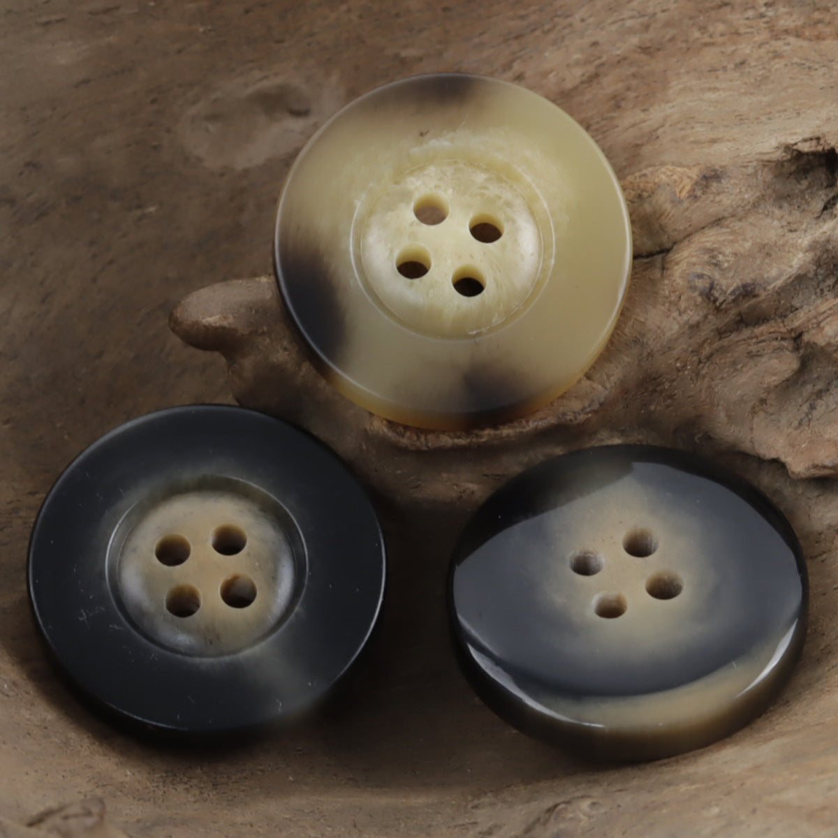 Light yellow-beige resin buttons with horn-like swirls and 4 holes, wide rim