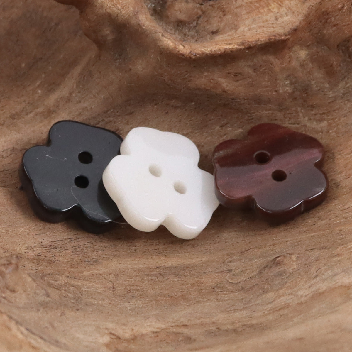 Two-hole flower resin buttons in dark, white, and brown tones on a wooden surface