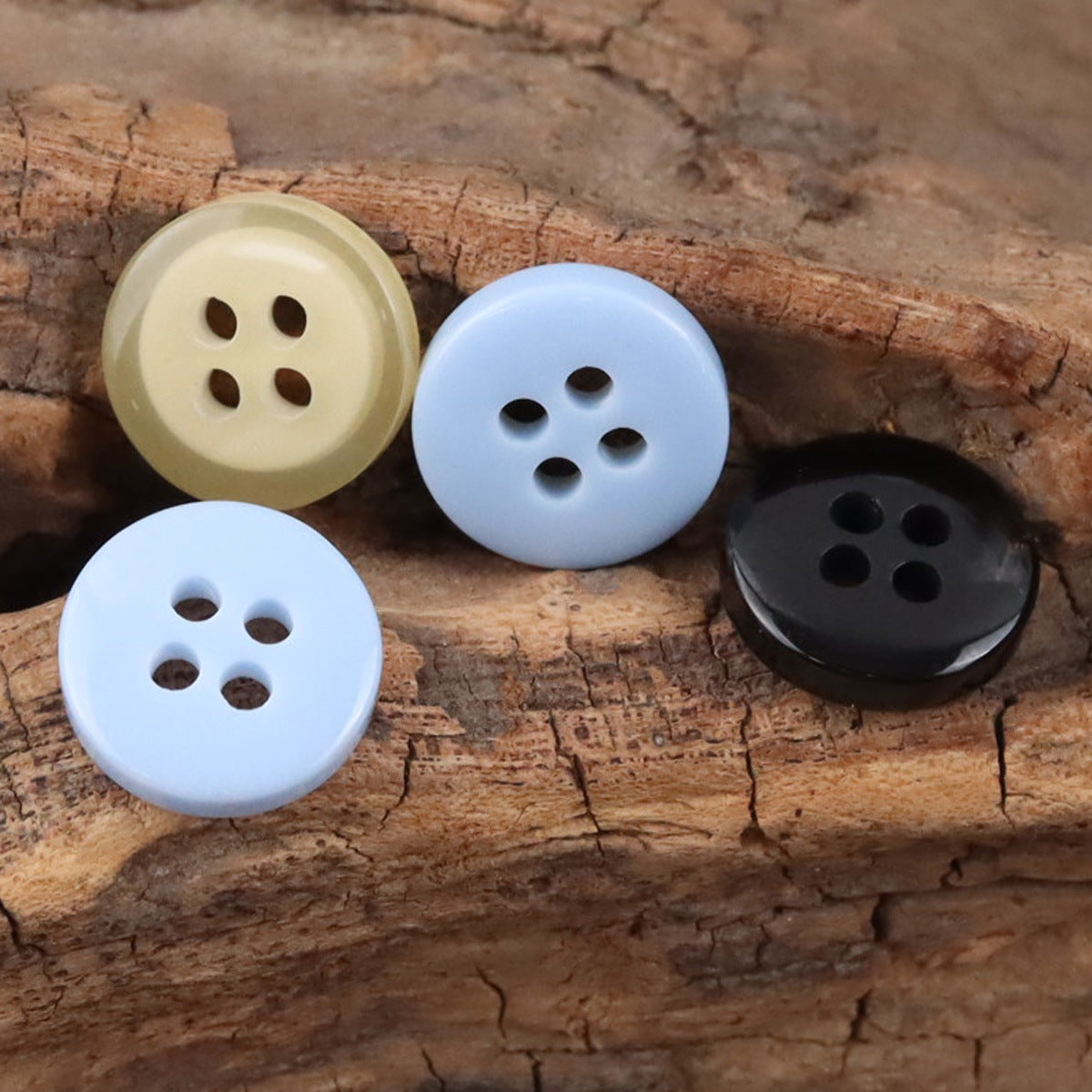 4-hole resin buttons in light blue, cream, yellow, and dark blue on wood