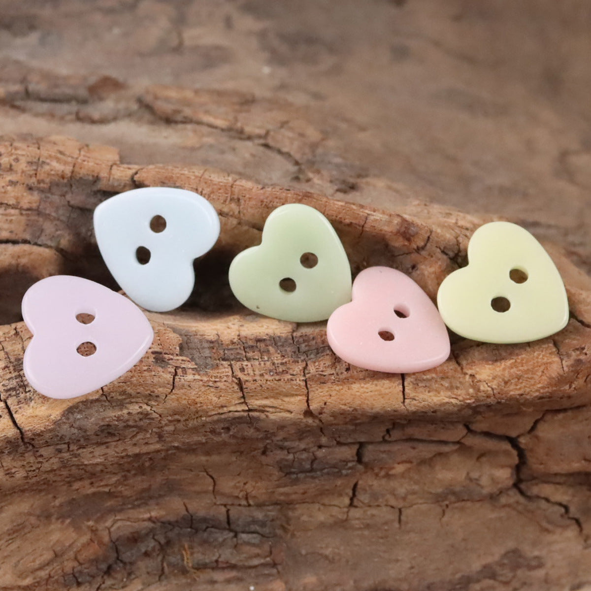 Ceramic heart buttons in white, pale green, pale yellow, and pink on a wooden surface.