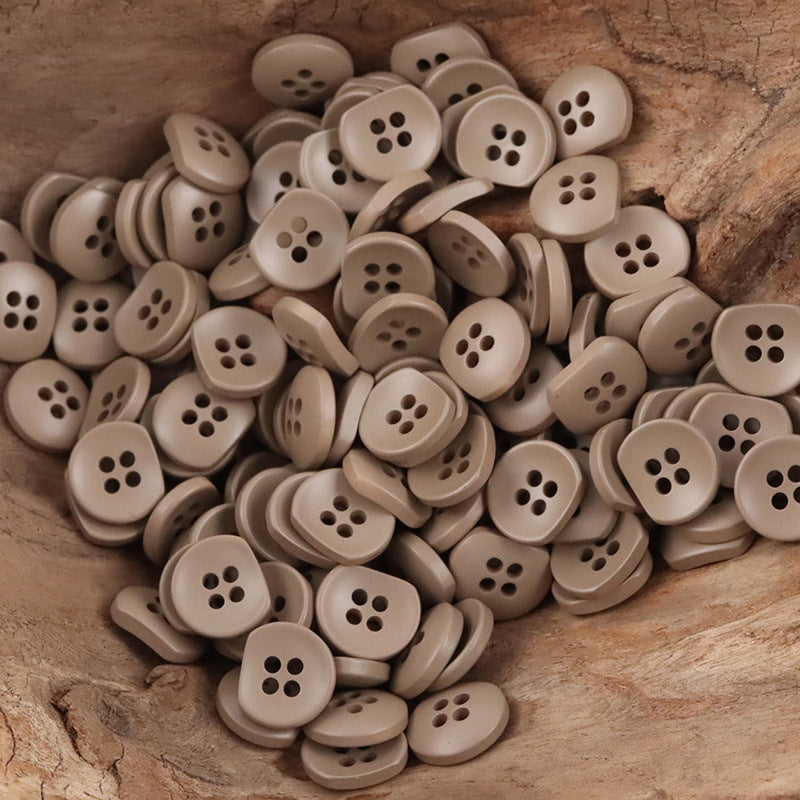 Bulk beige semi-circular resin buttons with four holes, stack-and-spread on wood