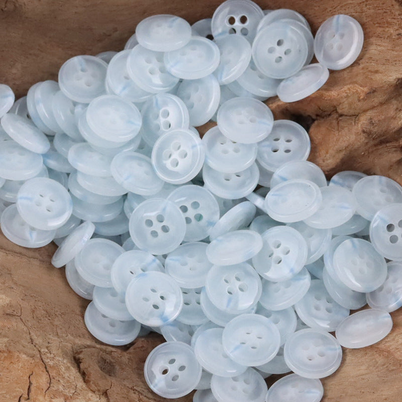 Pile of semi-transparent resin shirt buttons, light blue, four-hole design