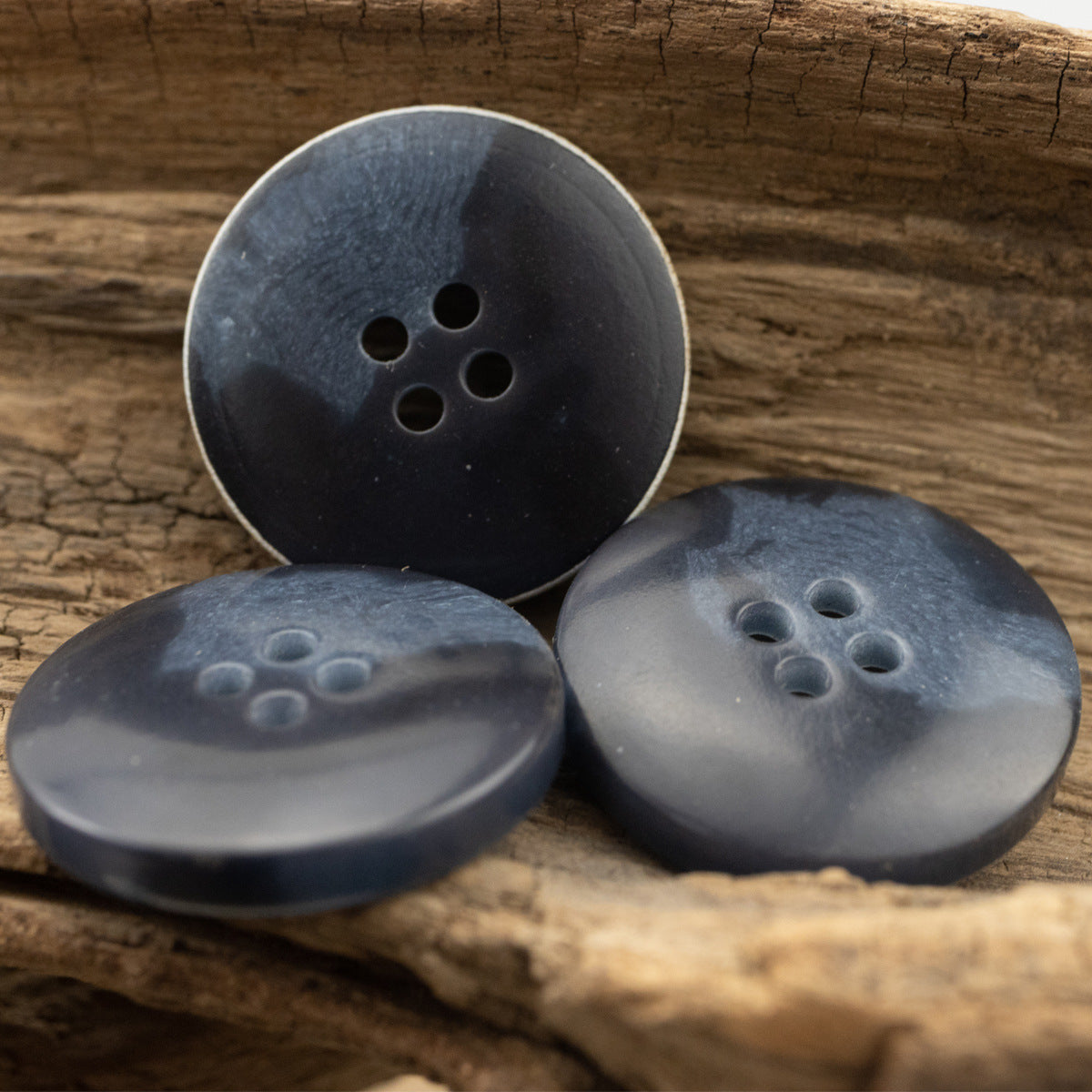 Dark blue urea buttons with four holes, shown on fabric and wood surface