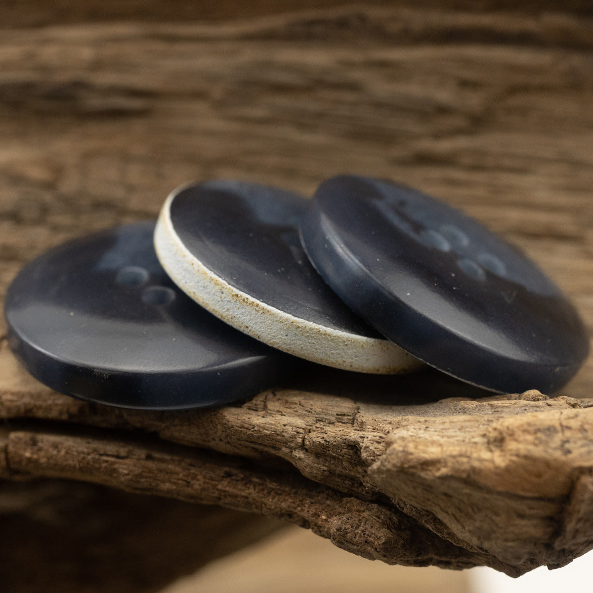 Pair of dark blue four-hole urea buttons, side view on wooden background