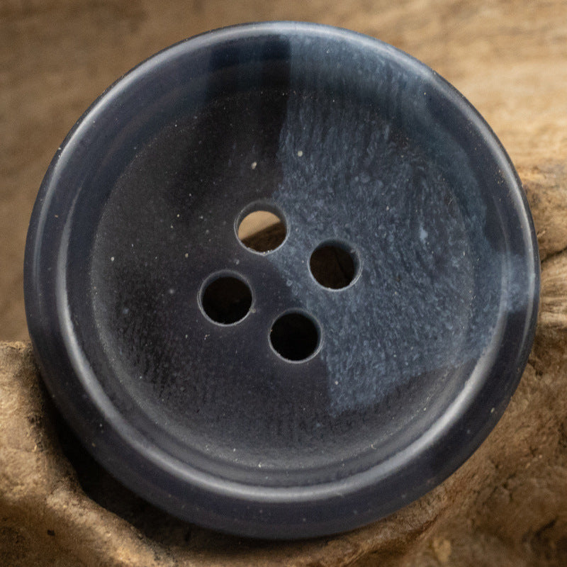 Dark blue four-hole urea button close-up, round face with wear marks